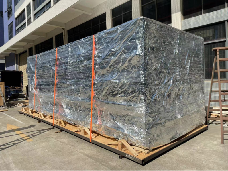 Fully wrapped industrial mold on a pallet outdoors, secured with orange straps and protected from environmental exposure before loading onto transport vehicle.