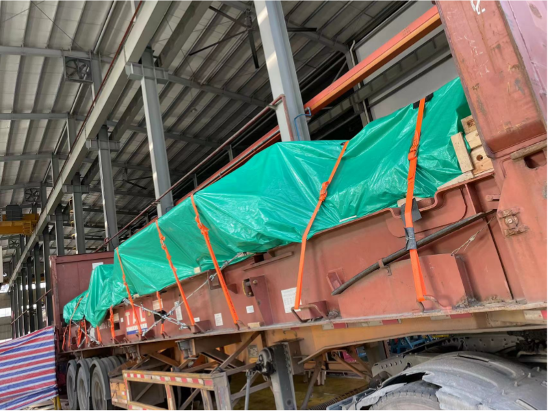 Oversized industrial mold covered with green tarp and secured with orange straps on a lowboy trailer, prepared for multi-modal transport.
