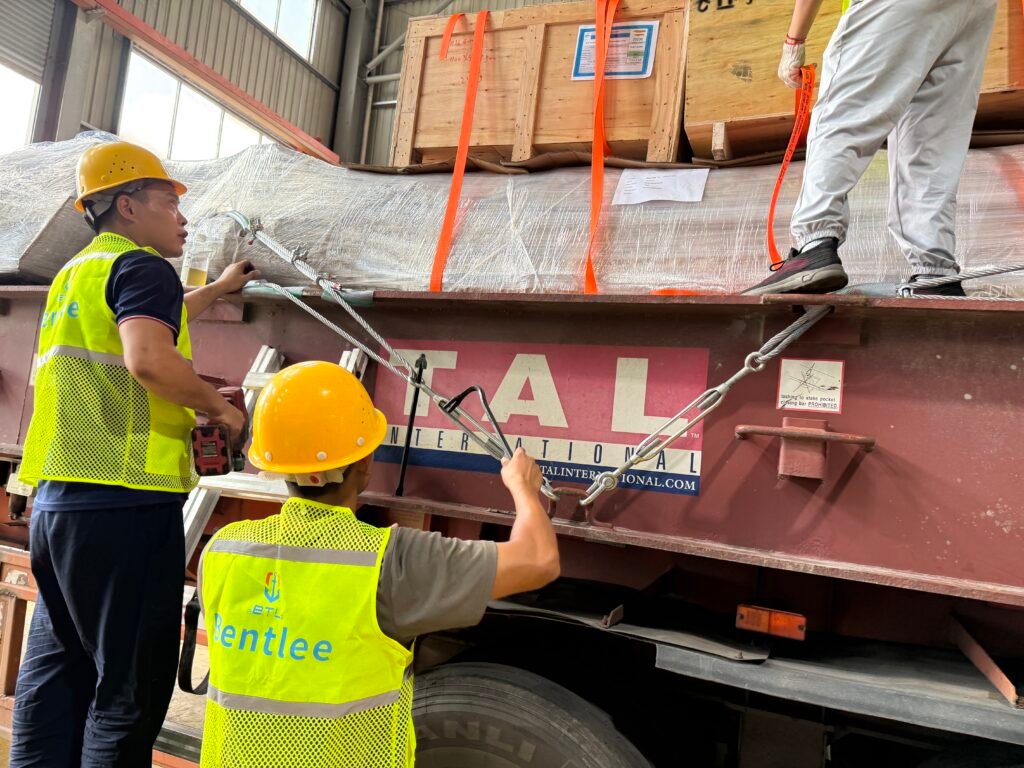 Workers tightening wire ropes and chain fittings on a flat rack container before shipment