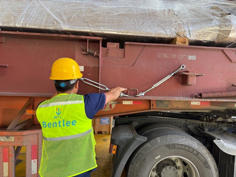 Close-up of a worker adjusting a turnbuckle on a steel wire lashing to maintain proper tension and prevent loosening during sea transport vibration.
