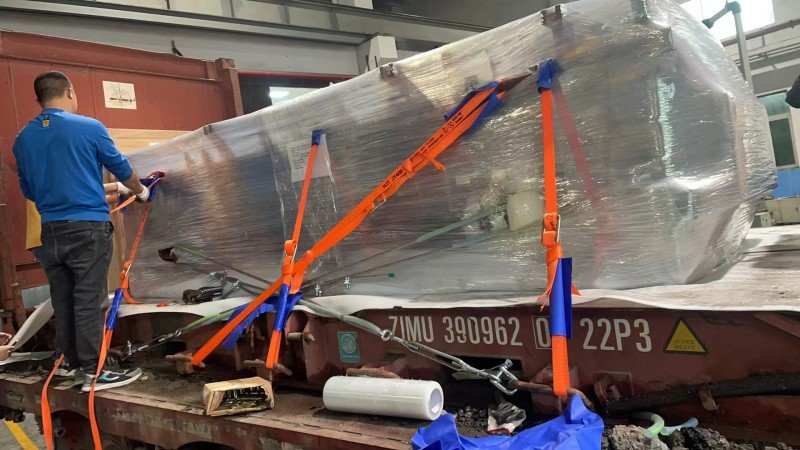 Worker securing oversized cargo with orange lashing straps inside a flat rack container during pre-shipment preparation