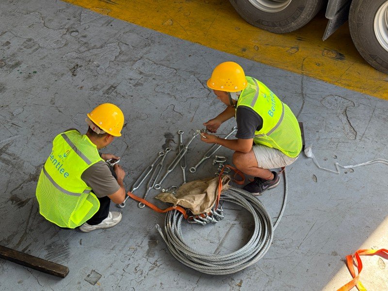 Workers preparing wire ropes, turnbuckles, and tools on the ground, illustrating the planning phase of an integrated cargo securing system involving lashing, blocking, and bracing.