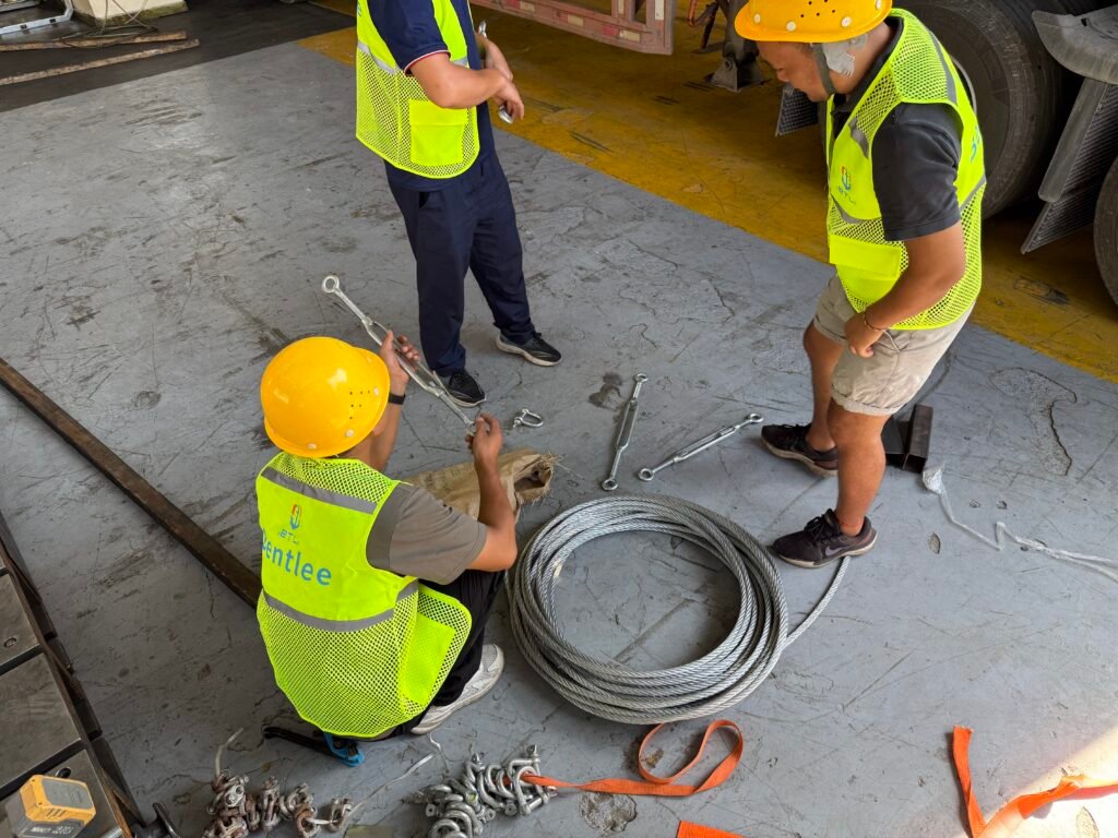 Workers inspecting wire ropes, turnbuckles, and shackles before loading oversized cargo onto a flat rack or open top container