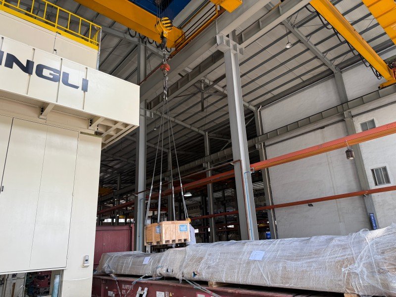 Crane lifting a wooden crate onto a flat rack next to long wrapped cargo, illustrating the importance of early securing planning and proper loading sequence in project logistics.