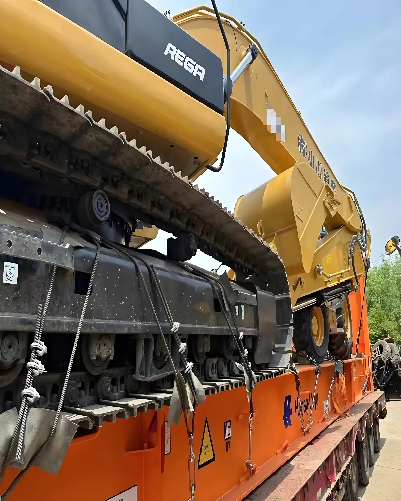 Close-up detail of heavy-duty steel chains and tensioners securing the tracks of a REGA excavator to the flat rack base to prevent movement during transit.