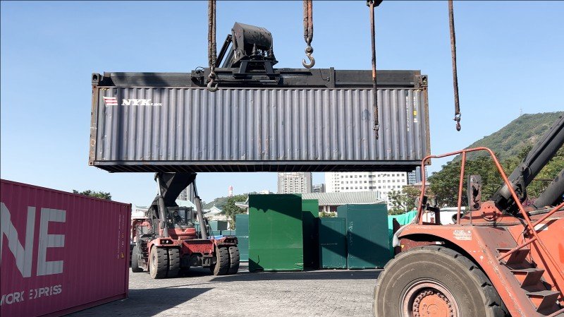 NYK shipping container being lifted by crane at port terminal with forklift support for secure positioning