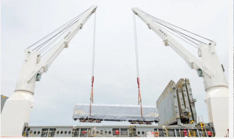 Two ship cranes lifting oversized cargo covered in tarpaulin for secure placement on deck