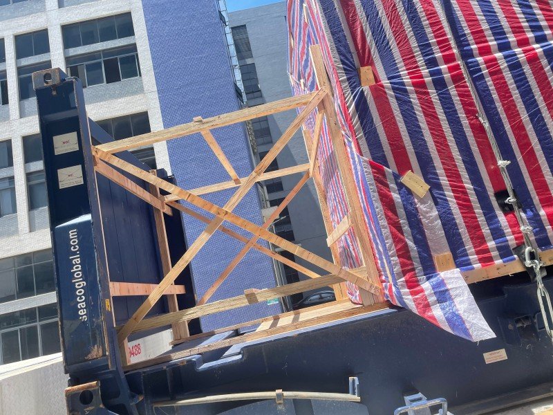 Close-up view of timber bracing structure and chain lashing angles on an open top container, showing securement points and wooden support frames for heavy cargo.