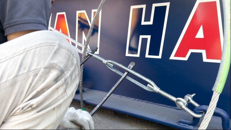 Worker tightening wire rope with turnbuckle on container corner fitting during OOG cargo securing process