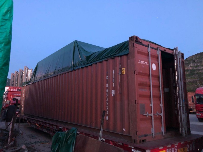 External view of a loaded 40ft open top container covered with green tarpaulin, ready for dispatch after verifying weight distribution and lashing compliance.