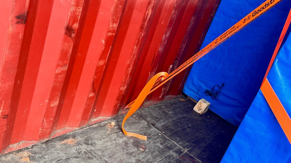 Flat rack container loaded with oversized machinery secured by orange lashing straps, demonstrating out-of-gauge (OOG) cargo handling
