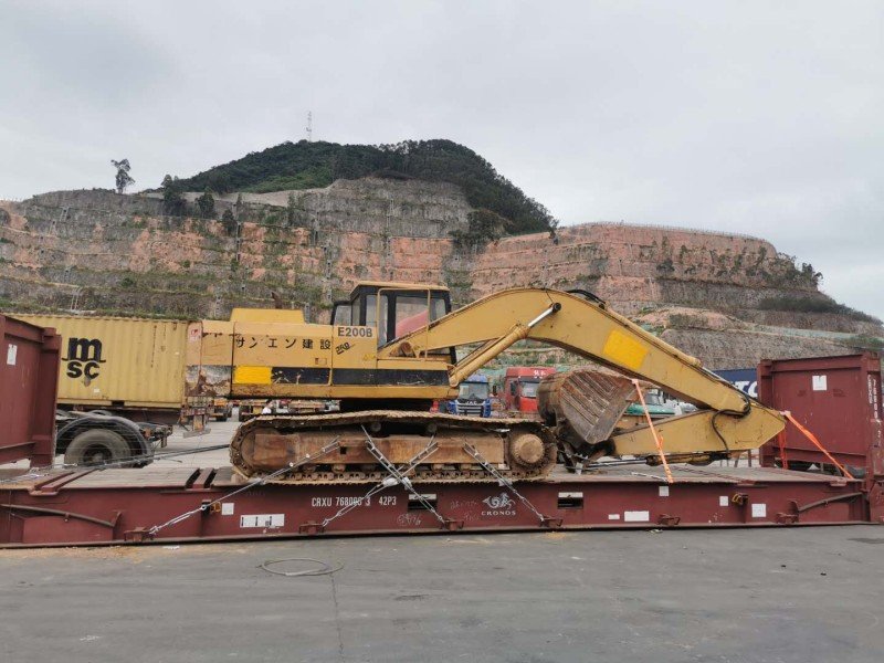 A crane lifts tall industrial equipment into an open top container, showcasing top-loading capability for cargo exceeding standard container height.