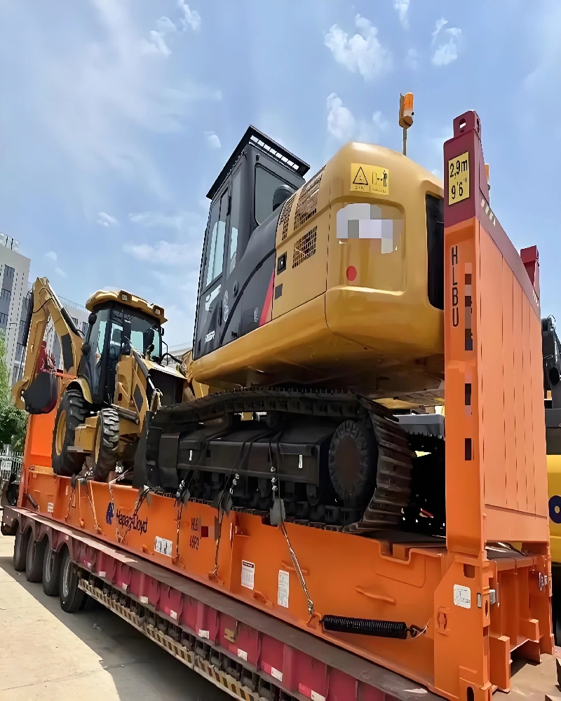 Side profile of a fully secured excavator and backhoe loader on a flat rack trailer, displaying height warning signs and Hapag-Lloyd branding, prepared for oversized cargo shipping.