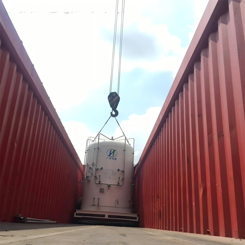 A large white cylindrical tank with "Guangdong Huaneng" logo is being carefully lowered by an overhead crane into a red open top shipping container, viewed from inside the container looking upward.