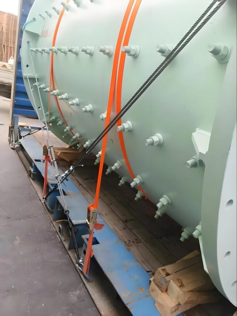 Close-up of orange lashing straps and steel wire ropes tensioned against a large green pressure vessel on a flat rack container, demonstrating the combination of securing materials used to resist acceleration forces during ocean transport.