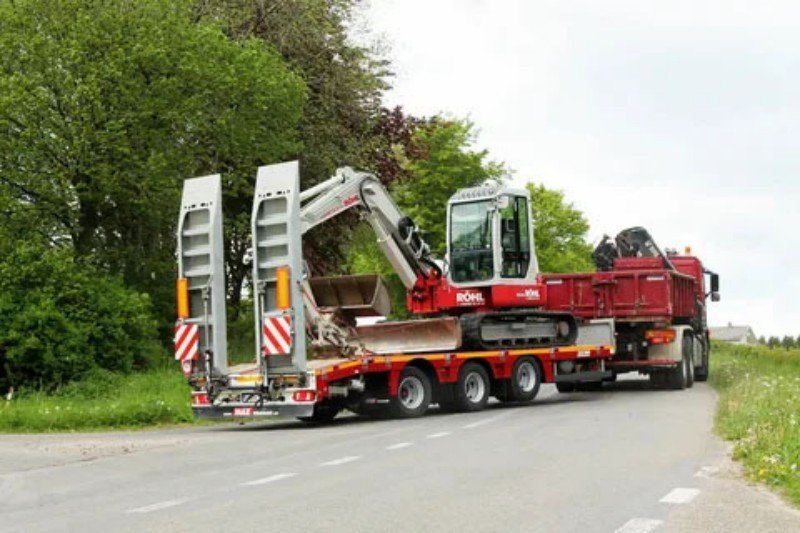 Red excavator being transported on a specialized low loader trailer highlighting weight distribution and center of gravity concerns for terminal crane safe working load limits
