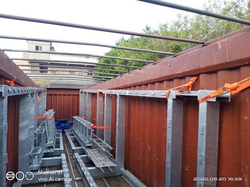Steel truss structures arranged horizontally inside open top container with orange straps securing cargo for transport