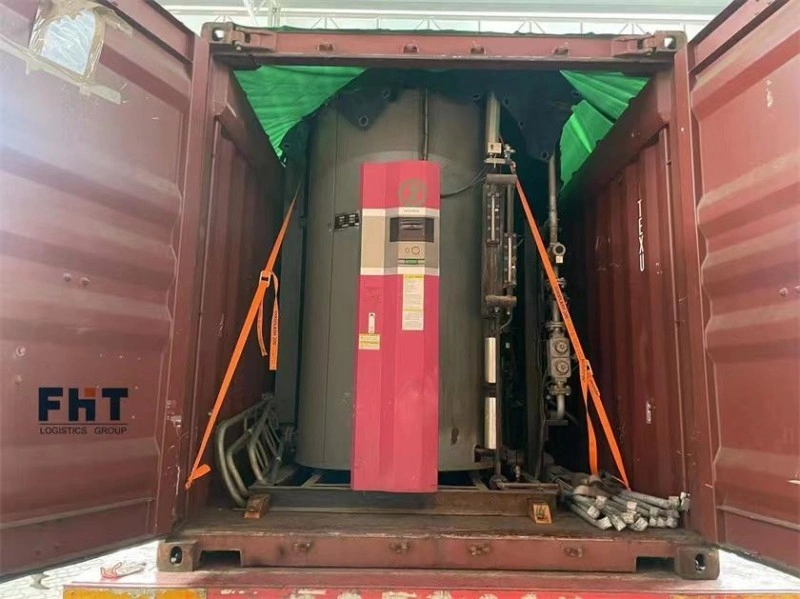 A large industrial boiler secured with orange lashing straps inside a red open top shipping container, with green tarpaulin covering the top for weather protection.