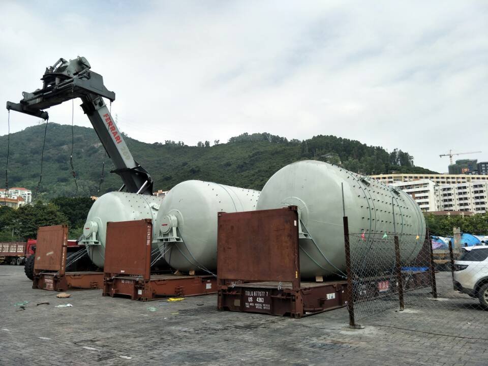 Multiple large industrial tanks being loaded into open top containers using a mobile crane at port yard
