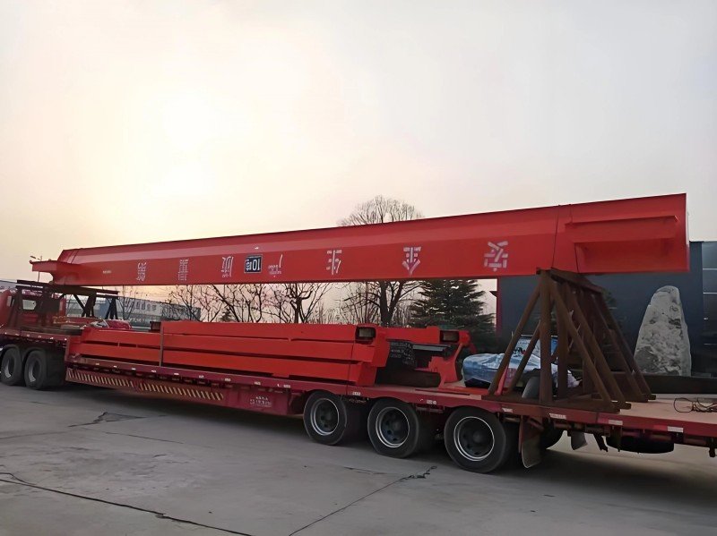 An extra-long red steel beam loaded onto a low loader truck extending beyond the trailer length, representing dimensional cargo that exceeds standard limits and requires specific routing and escort vehicles.