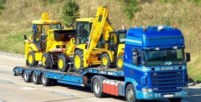 Blue truck transporting multiple yellow backhoe loaders on a flatbed illustrating complex stowage planning and non-stackable OOG unit requirements for vessel deck placement