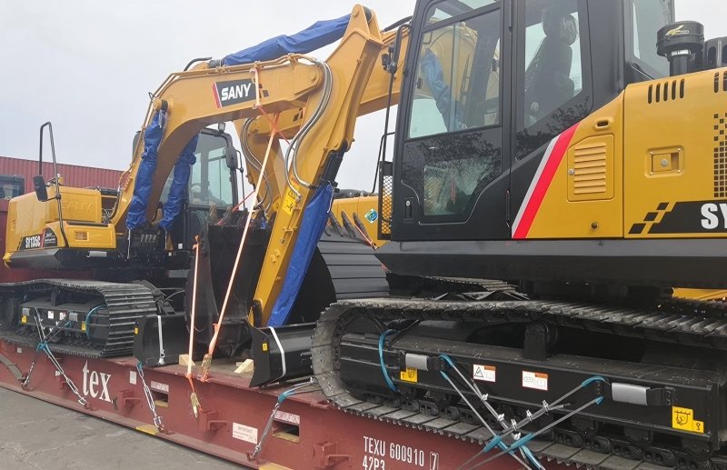 Two SANY excavators loaded on flat rack trailer with protective covers and chain lashing for secure transport