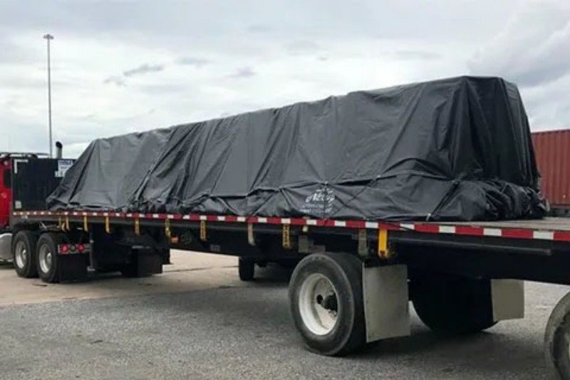 Long out-of-gauge cargo covered in black tarpaulin on a flatbed semi-trailer demonstrating rear overhang challenges and dimensional restrictions for port gate entry