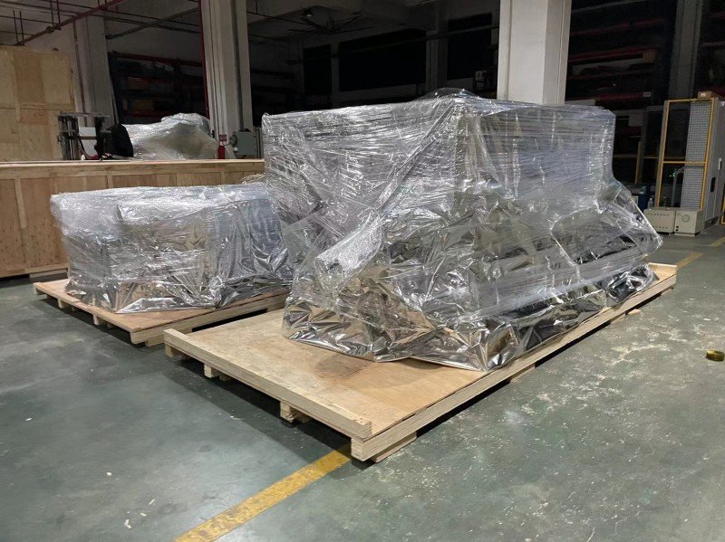 Industrial machinery wrapped in protective plastic film on wooden pallets before loading into open top container