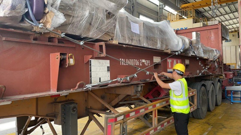 Worker securing heavy cargo with chain lashings and turnbuckles on open top container trailer