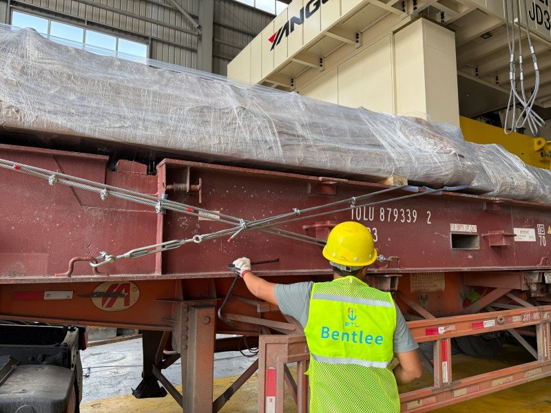 Workers in safety gear securing over-height project cargo on a TAL open top container flat rack, demonstrating engineered lashing plan execution and preliminary cargo assessment for OOG declaration compliance