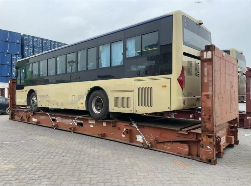 The rear perspective of a beige city bus loaded onto a flat rack container, showing the alignment of wheels, chassis support, and lashing points used to maintain balance and prevent movement during transit.