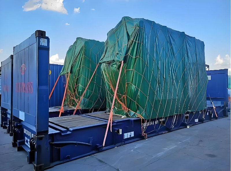 Two large units covered in green protective netting loaded onto a double flat rack configuration, illustrating the complexity of transporting high-profile cargo that requires detailed route planning.
