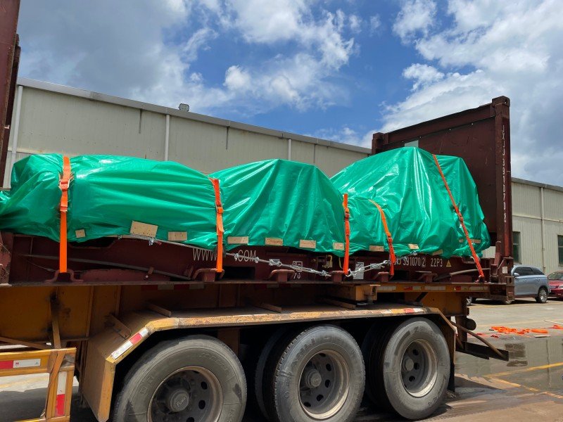 Oversized machinery secured with green tarpaulin and orange straps inside open top container for safe transportation