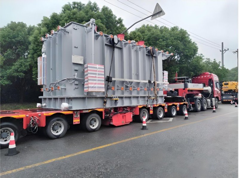 Oil-filled power transformer secured on red multi-axle trailer with anti-vibration pads and protective wrapping during road transit
