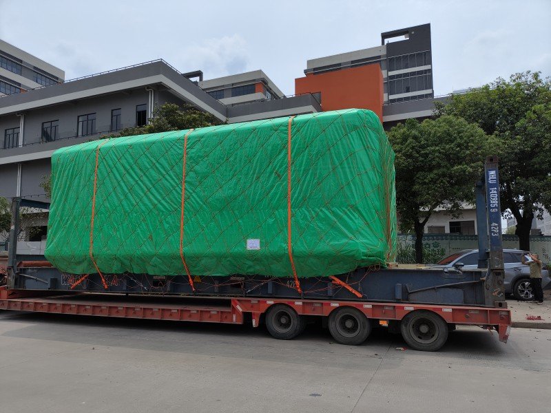 Oversized project cargo wrapped in green protective covering and secured with orange straps on a flatbed trailer, highlighting the importance of engineered lashing plans and verified gross mass (VGM) certificates for safe inland transport and carrier acceptance