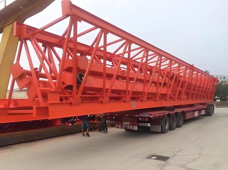 Close-up view of a large, irregular red steel framework secured on a flatbed truck, demonstrating the complexity of cargo lashing and blocking required for out-of-gauge shipments to ensure stability during transit.