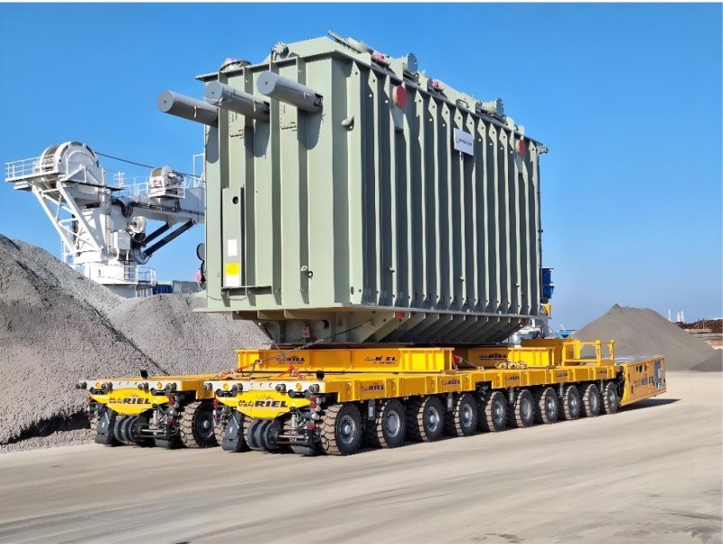 Massive power transformer transported on yellow SPMT (self-propelled modular transporter) at industrial site