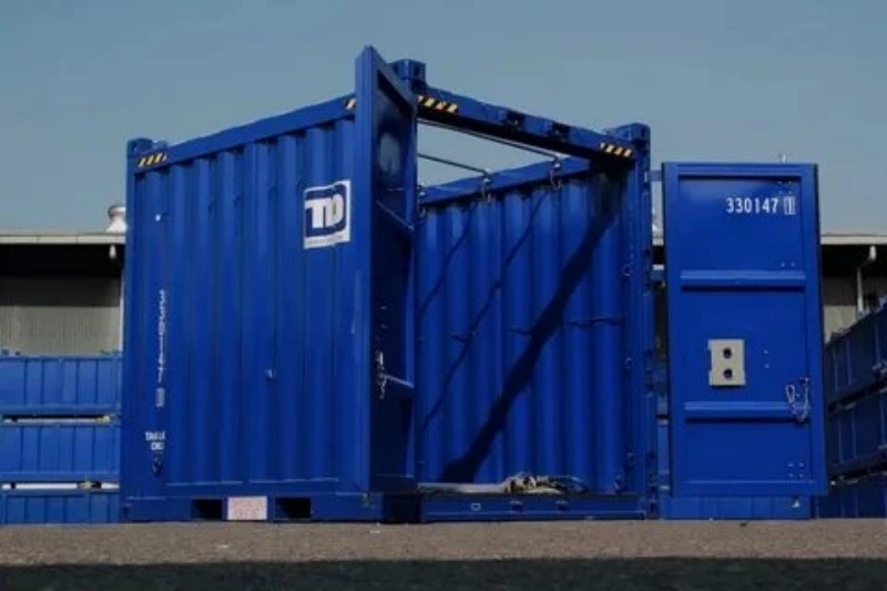Blue shipping container with fully open side doors providing wide access for loading oversized industrial equipment
