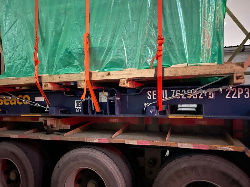 Wooden dunnage and steel beams under tarp-covered construction machinery to distribute weight evenly on container floor