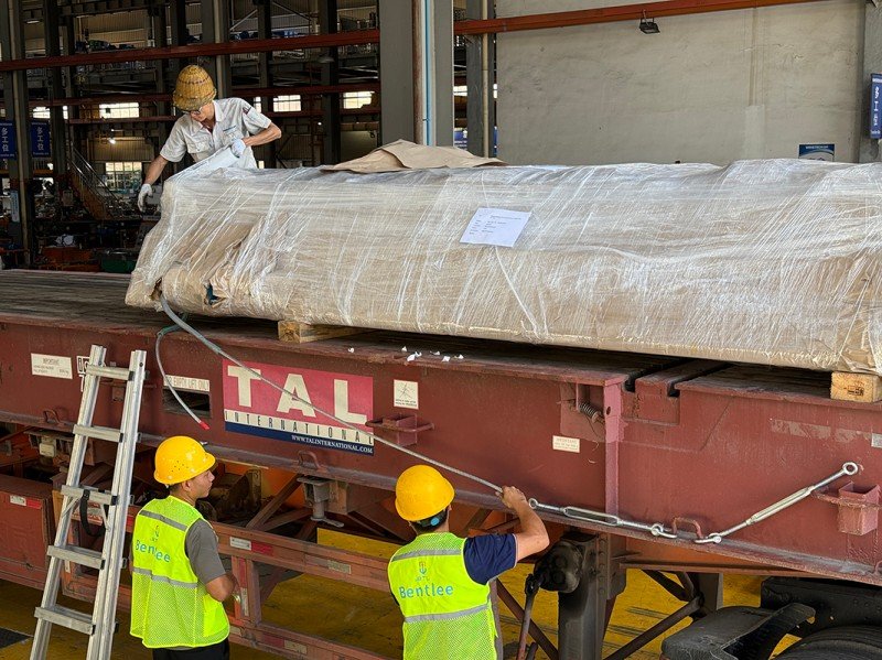 Multiple workers collaborating to secure oversized cargo on an open top container using various lashing techniques, emphasizing the need for comprehensive dimensional verification and terminal coordination for successful carrier approval