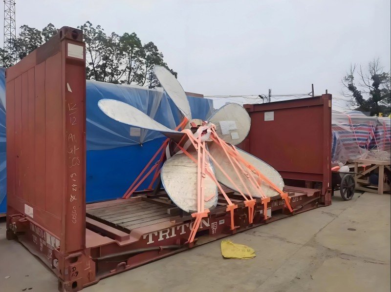Large wind turbine blades securely strapped onto a red flat rack container, illustrating the use of flat racks for transporting oversized renewable energy components.