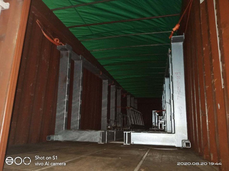 Tower crane sections securely loaded vertically inside open top container with green tarpaulin cover and orange lashing straps