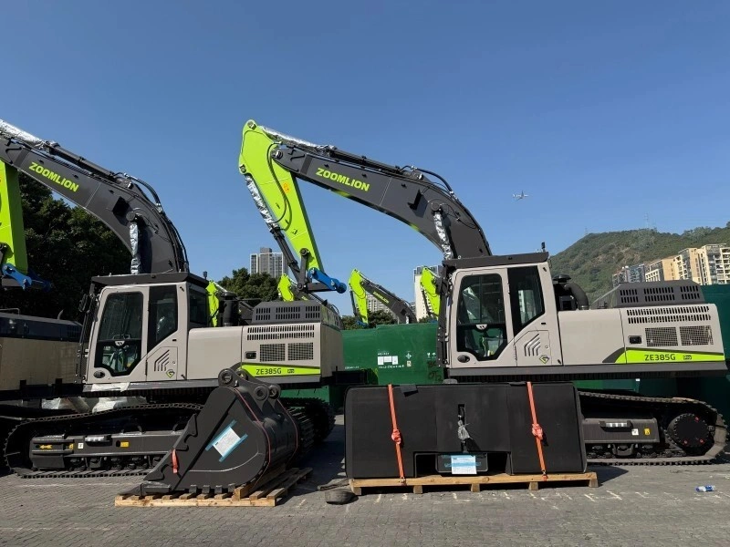 Two new grey and green Zoomlion ZE385G excavators are parked side-by-side in a yard, with their detached black buckets secured on wooden pallets in the foreground.