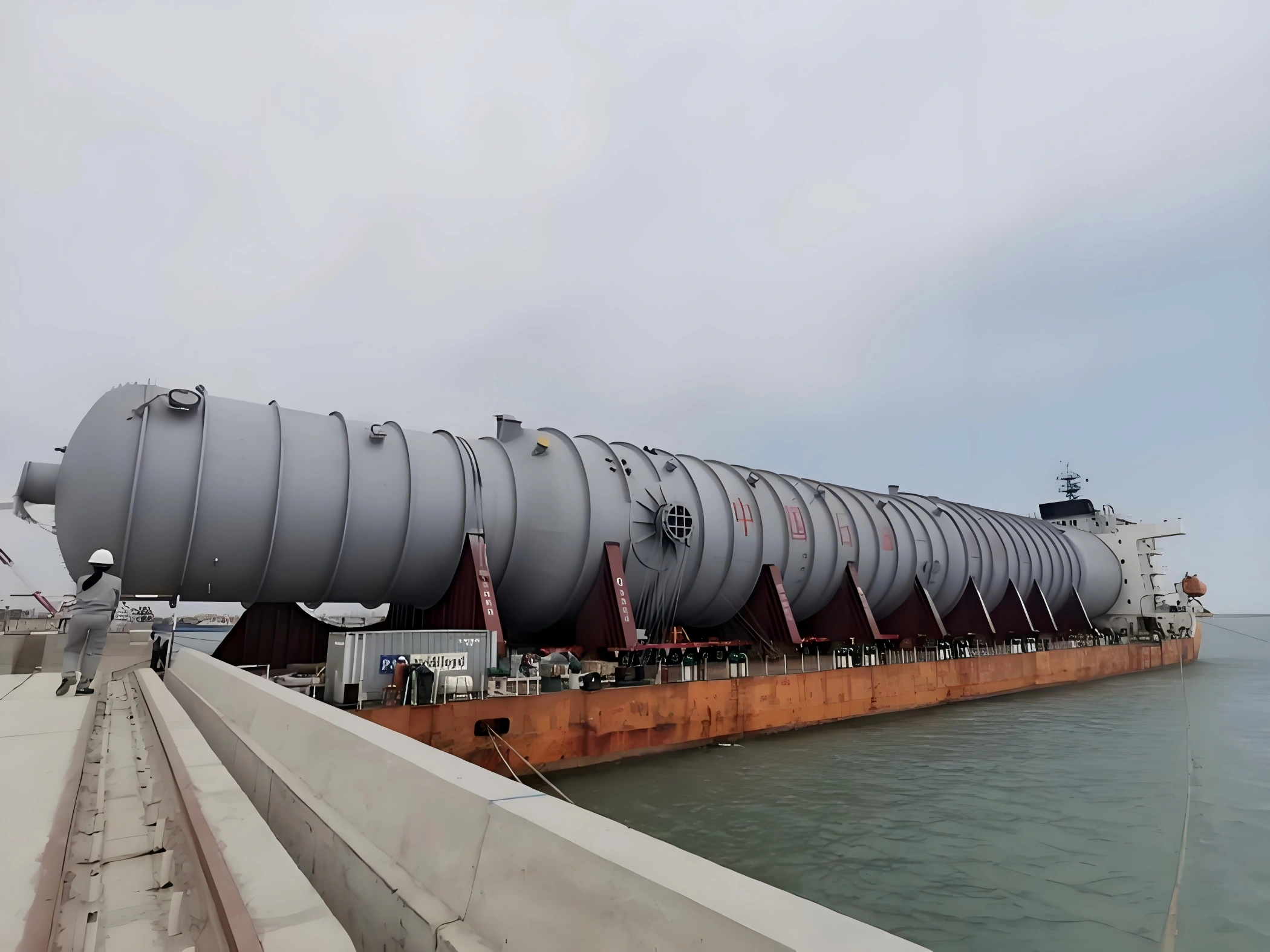 Multi-section industrial pressure vessel loaded on a barge for OOG shipment, supported by dunnage and securing brackets