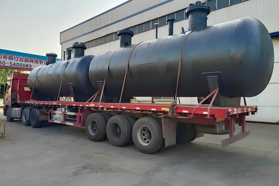Large black coated pressure vessel with multiple nozzles and flanges loaded on red flatbed trailer and secured with tension straps for refinery equipment transport