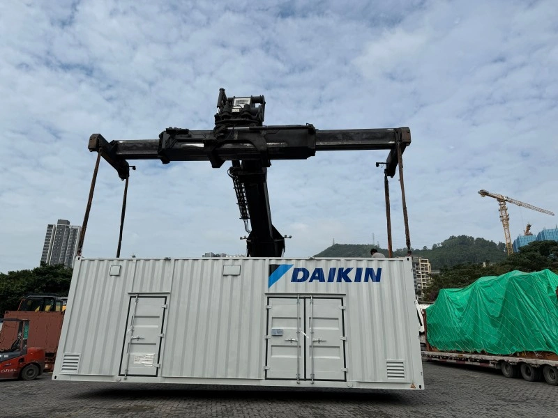 A large white Daikin container is suspended in mid-air by a heavy-duty port crane, demonstrating the lifting process for oversized industrial equipment. The scene highlights the critical role of proper rigging and crane capacity in OOG logistics.