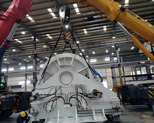 FLEXTech heavy industrial machine suspended by dual cranes during precision loading into open top container at factory site