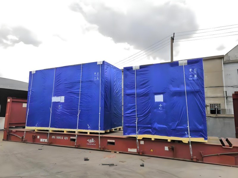 Two tarp-covered loads on flat rack — zero lateral containment, reliant only on vertical lashing.
