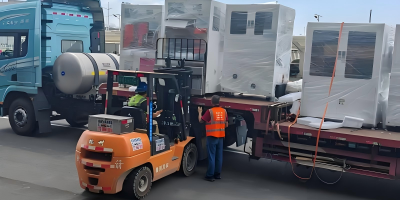 Orange forklift loading vacuum wrapped industrial equipment onto red flat rack with supervisor in safety vest for construction logistics operation