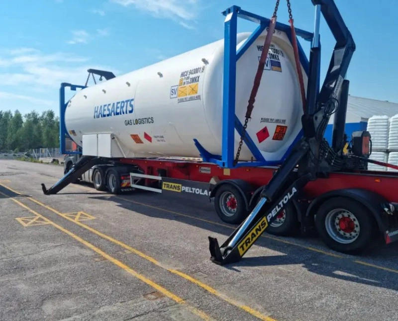 Haesaerts gas logistics tank container being loaded onto trailer by crane, marked with SV and hazardous material symbols